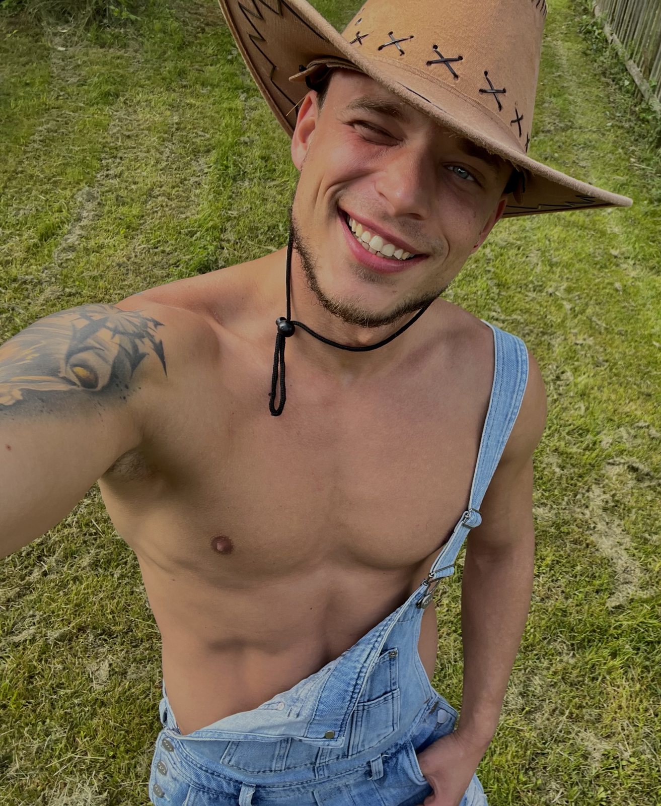 Pavlos smiling outdoors in overalls and a cowboy hat